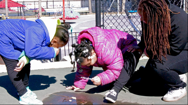 Kids and mom looking at puddle with lens