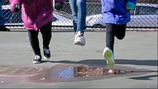 Three girls jump puddle